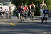 Eine Gruppe von Menschen nimmt an einer Outdoor-Aktivität auf einer Strasse teil. Die meisten fahren Fahrrad, während eine Person in der Mitte Inlineskates trägt. Alle tragen Helme und sportliche Kleidung. Die Strasse ist mit gelben Linien markiert, und im Hintergrund sind Bäume und Gebäude zu sehen.  Eine Gruppe von Menschen nimmt an einer Outdoor-Aktivität auf einer Strasse teil. Die meisten fahren Fahrrad, während eine Person in der Mitte Inlineskates trägt. Alle tragen Helme und sportliche Kleidung. Die Strasse ist mit gelben Linien markiert, und im Hintergrund sind Bäume und Gebäude zu sehen.